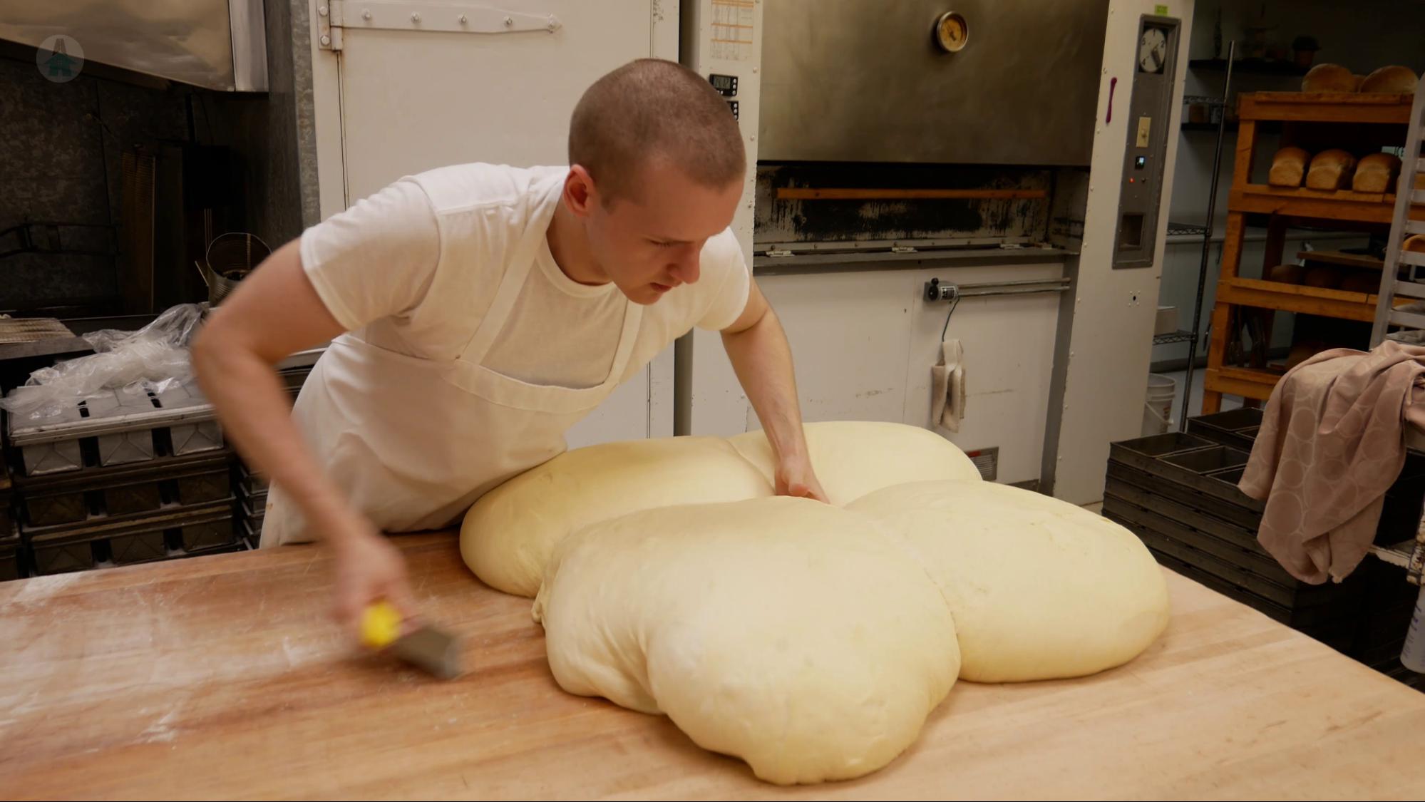 After rising, the donut dough is cut into four sections before it is gently patted to remove excess air and allowed to rest.